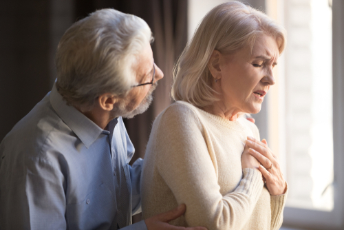 Close-up focus on elderly wife hold hand on breast touch chest having heart attack.