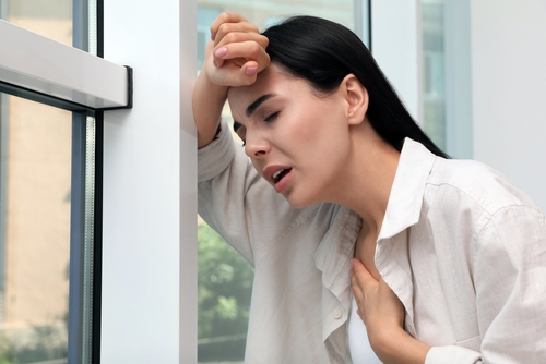 Young woman suffering from breathing problem near window indoors