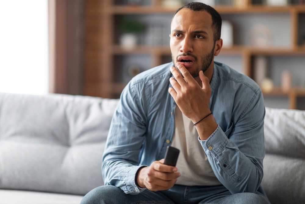 Confused Young African American Guy Watching Tv Show In Living Room