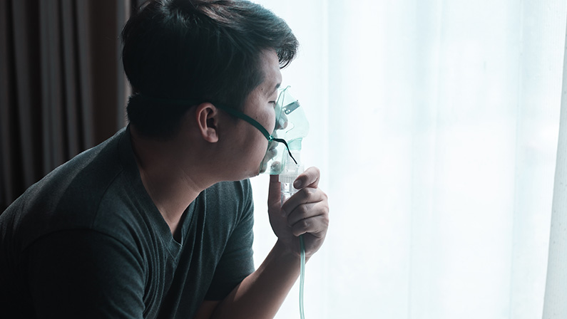 Panoramic shot of asthmatic man using inhaler with spacer. Fat man using asthma inhaler while sitting at home due to allergy. Asia man using spray asthma