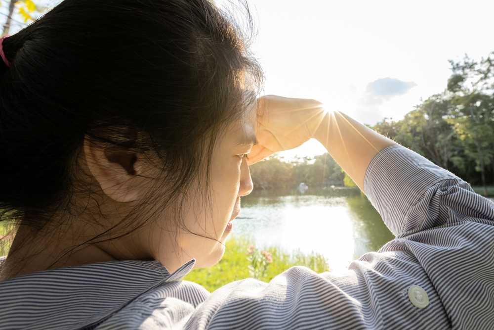 young female covering face by hand of- bright sun in outdoor on sunny day, feel dizzy