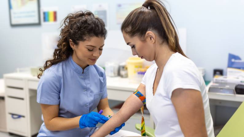 Preparation for blood test with young woman by female doctor in medical uniform.