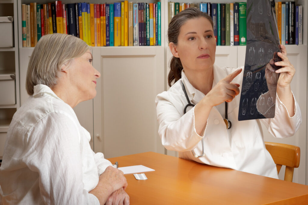 Experienced doctor in white coat showing her female patient on an image of ct-scan