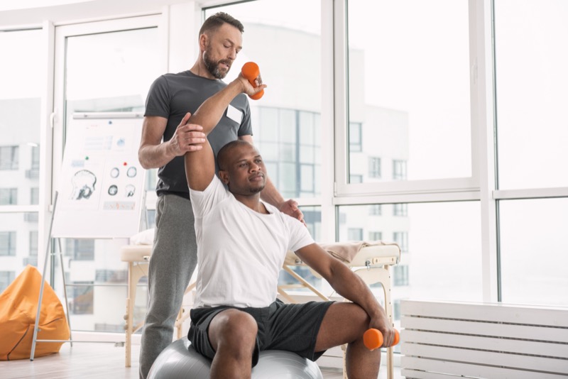 Sports therapy. Pleasant good looking man exercising with dumbbells while being in the gym