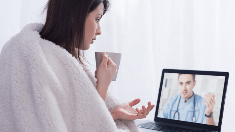woman covered with thick blanket, holding a white cup during on-line consultation